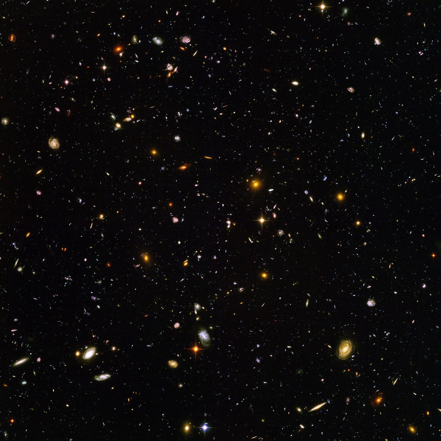 A deep black field scattered with thousands of faint coloured smudges, spirals and ellipses — each one a distant galaxy, photographed by the Hubble Space Telescope