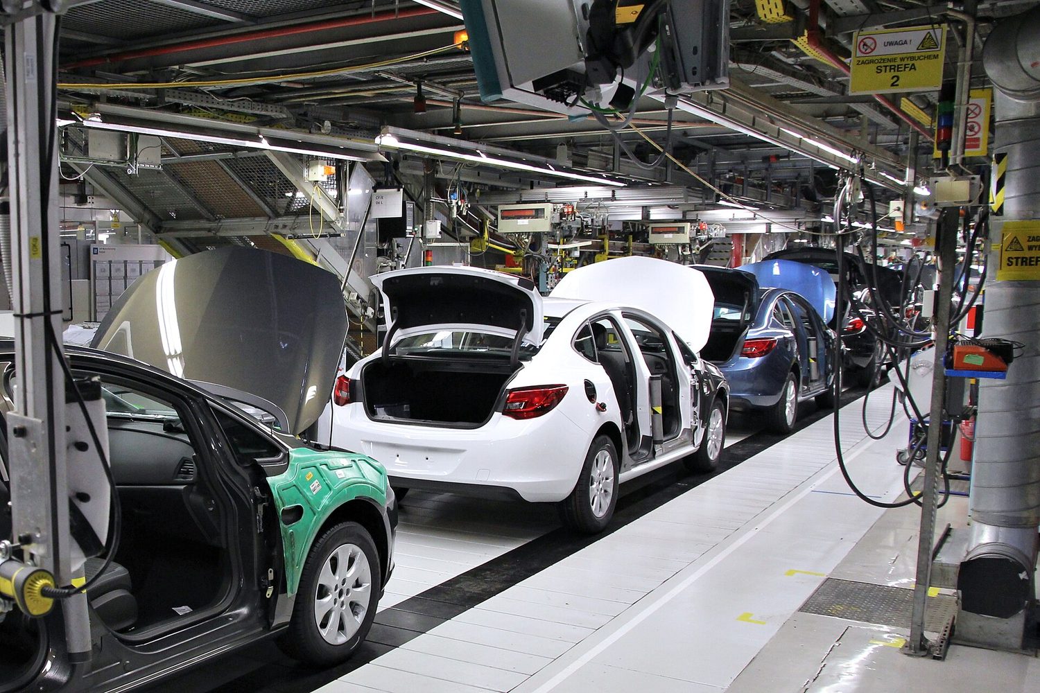 A car assembly line inside a factory: part-built cars in sequence along a moving line