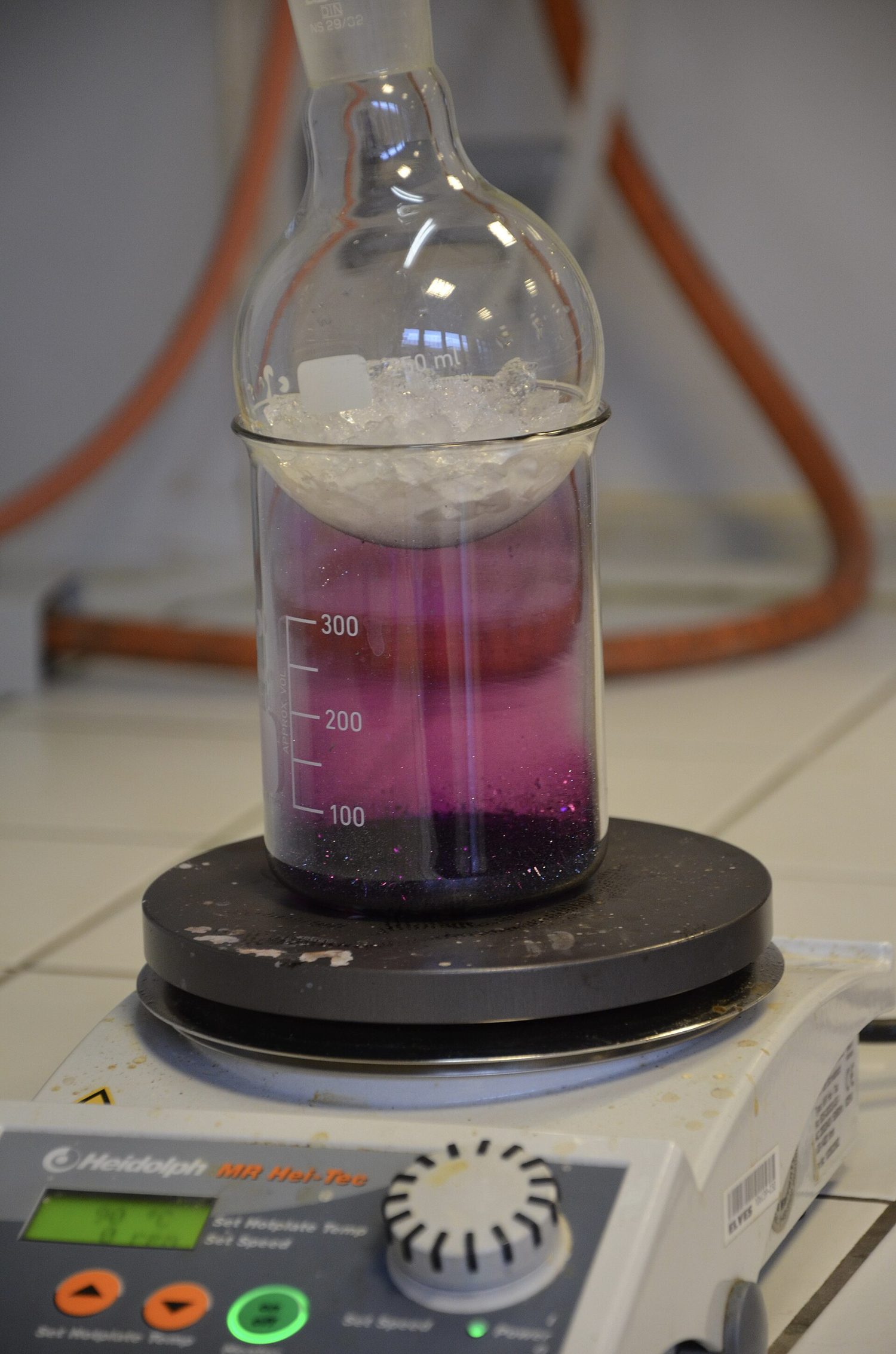 A beaker of solid iodine on a hotplate filled with bright purple iodine gas, with a flask of ice resting on top where the gas turns back to a solid