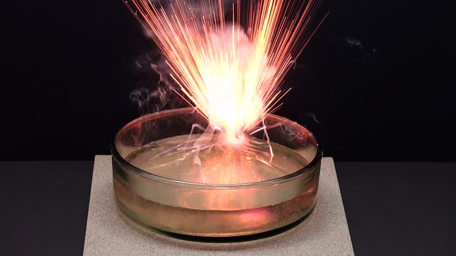 A small piece of potassium burns with a bright burst of sparks and a lilac flame on the surface of a dish of water