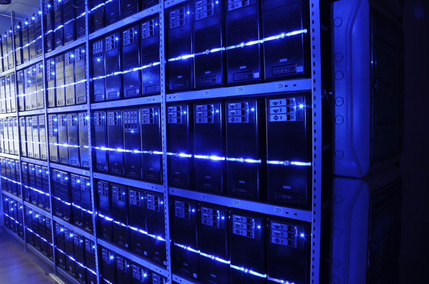 Long rows of computer servers in metal racks, lit with blue lights, inside a data centre