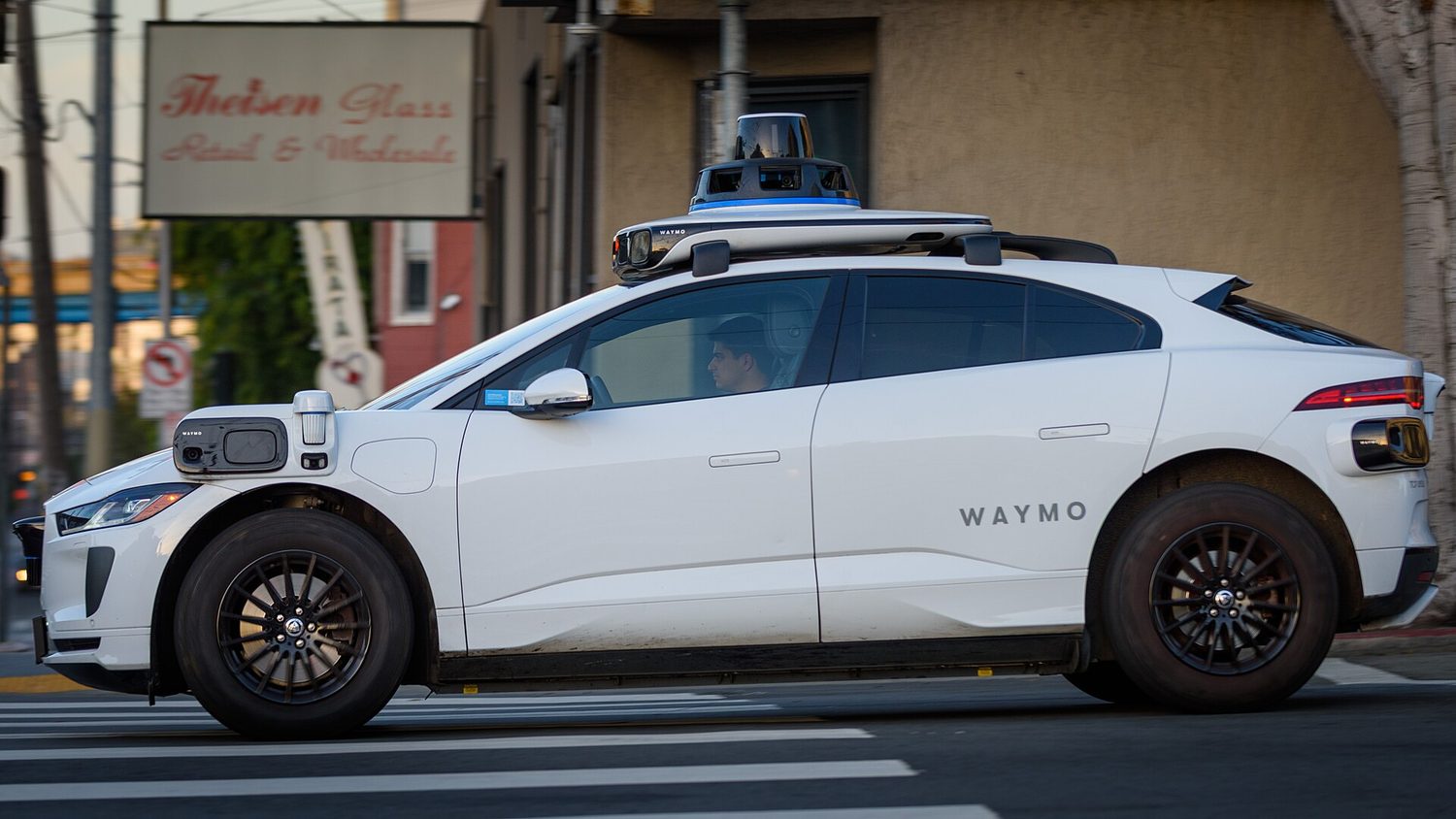 A small white self-driving car on a road, with a spinning sensor on its roof