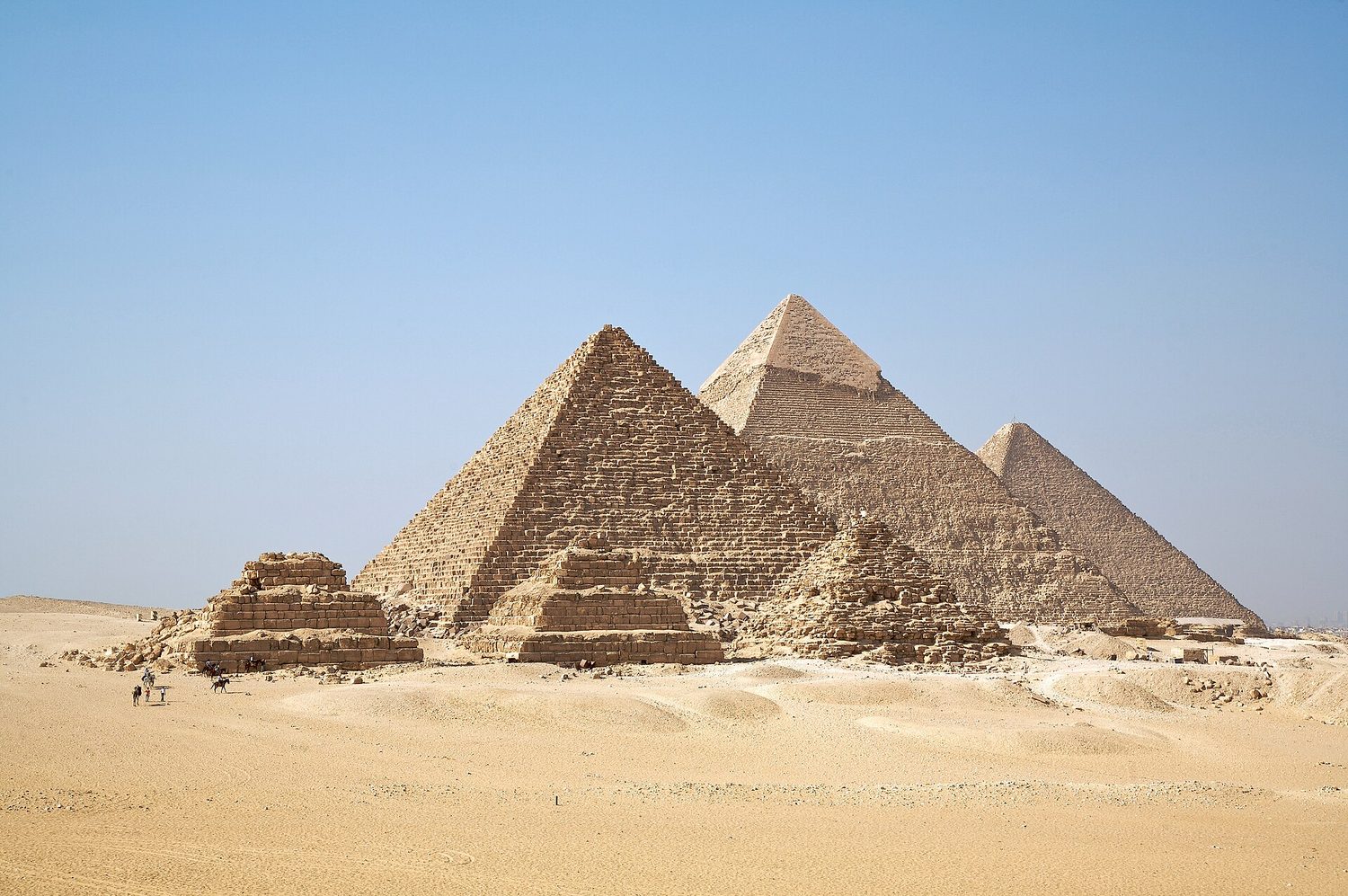 The three pyramids of Giza in the desert under a blue sky