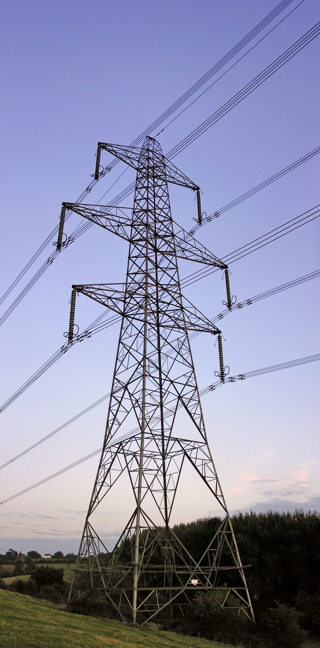A tall steel lattice pylon carrying many cables across the countryside against an evening sky