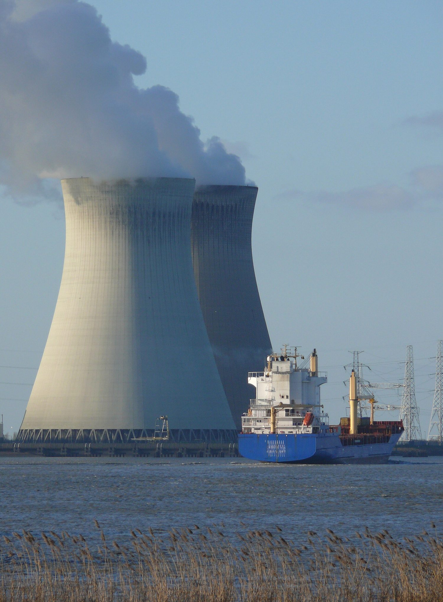Two large cooling towers of a nuclear power station beside a river, giving off white clouds of steam