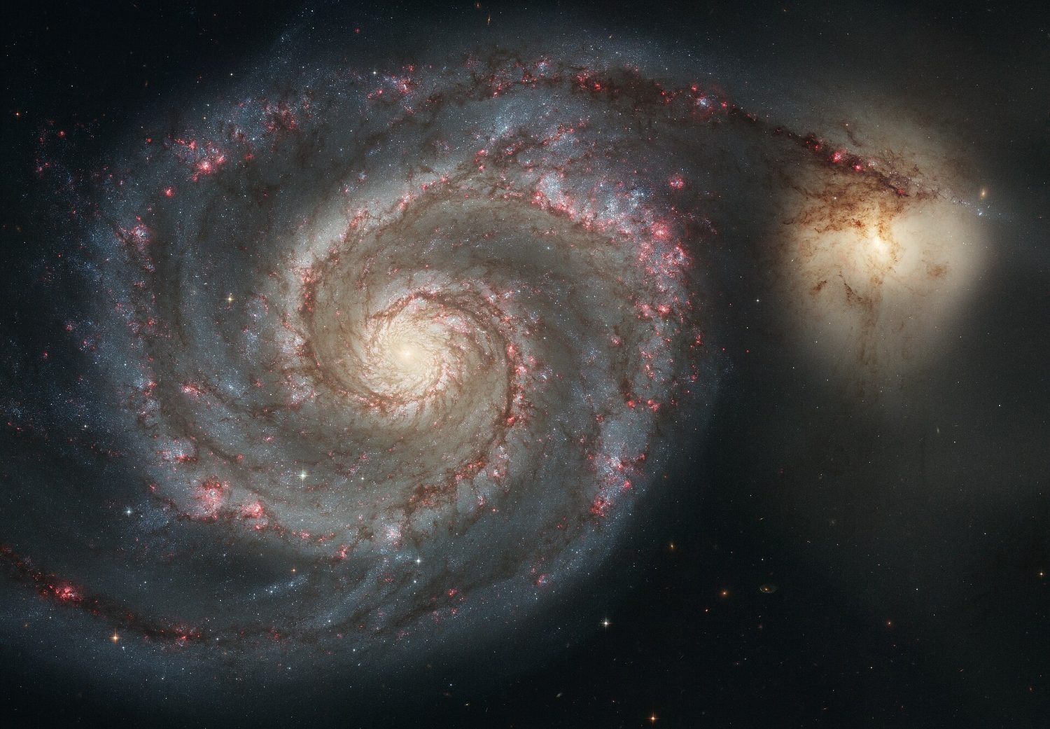 A spiral galaxy seen face-on, with curved arms of stars winding out from a bright centre and a smaller companion galaxy at the edge